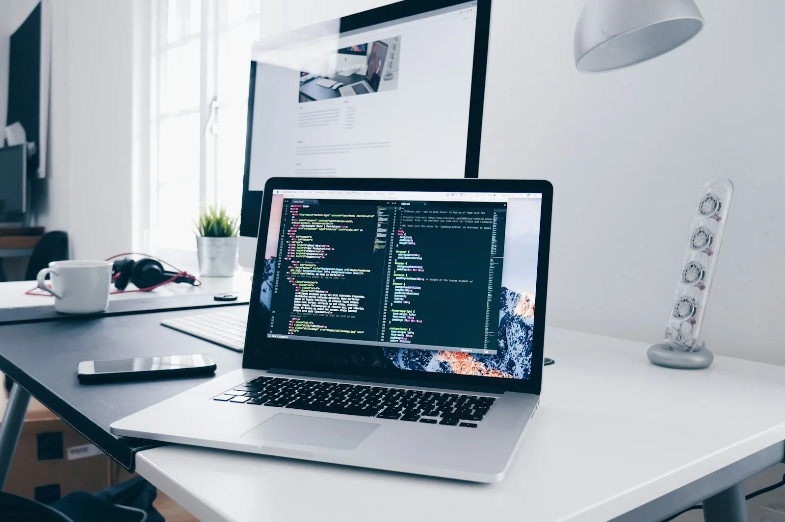 Postazione con laptop e schermo che mostrano codice e anteprima di un sito